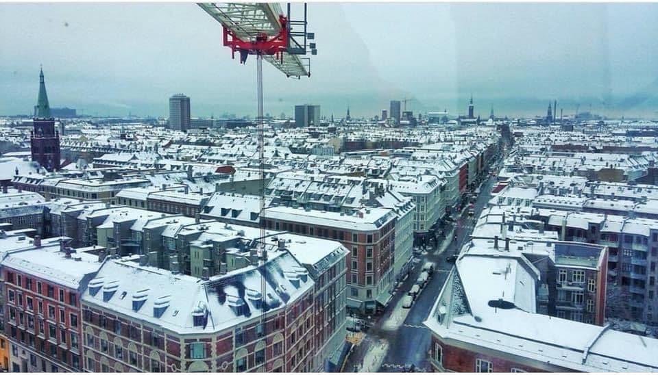 A tower crane rising above a snow-covered cityscape, seen from a birds-eye view.
